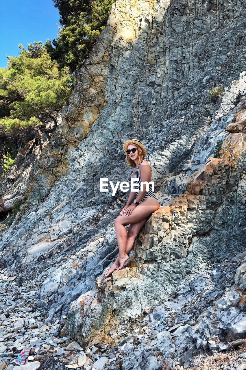 Low angle view of young woman in swimwear sitting on rocks
