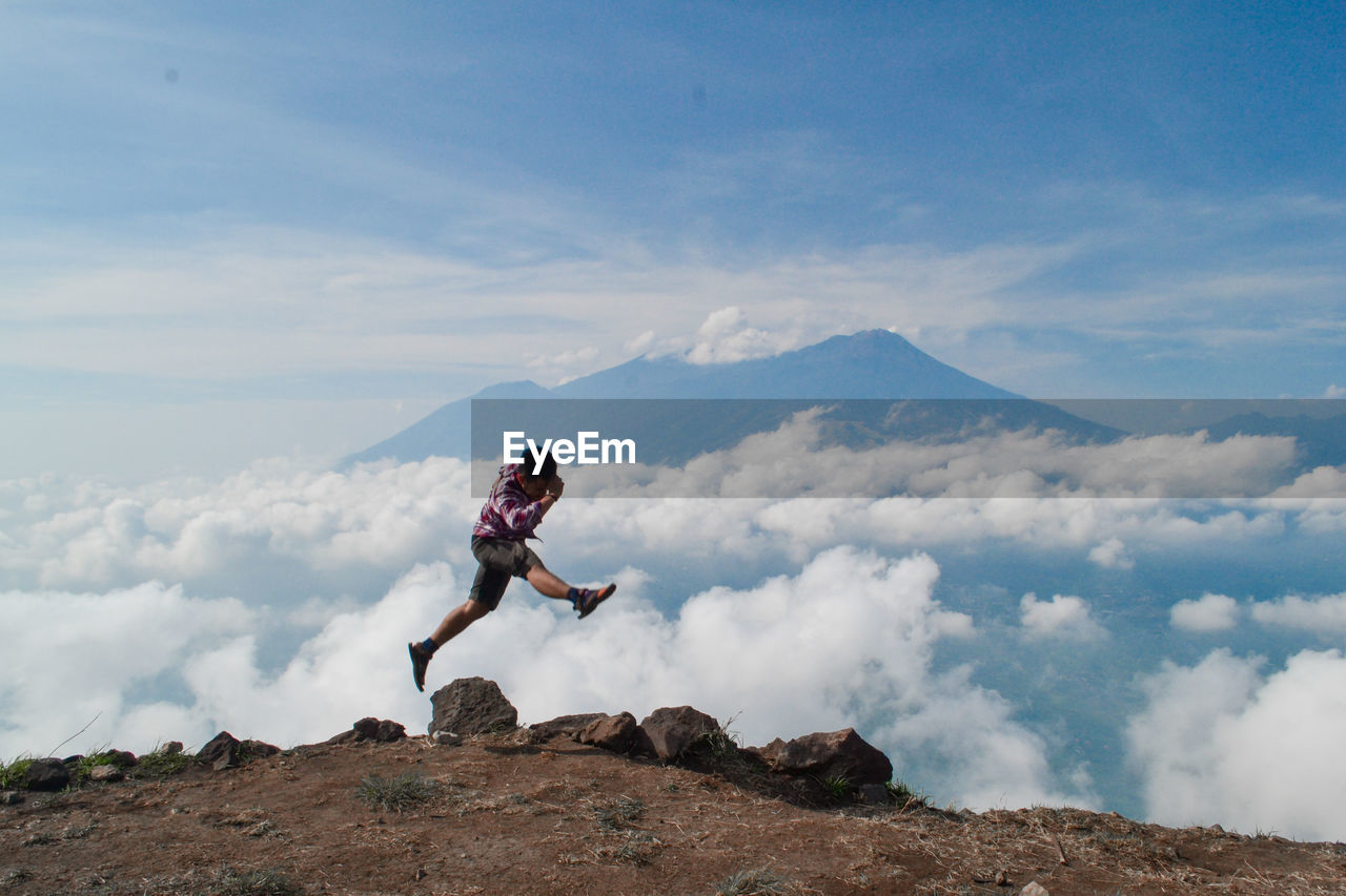 Full length of man jumping on mountain peak against sky