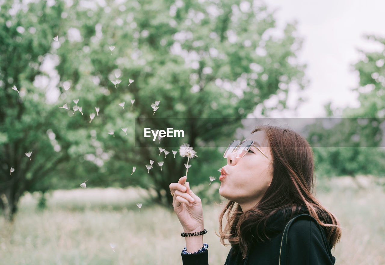 Beautiful woman blowing dandelion at park