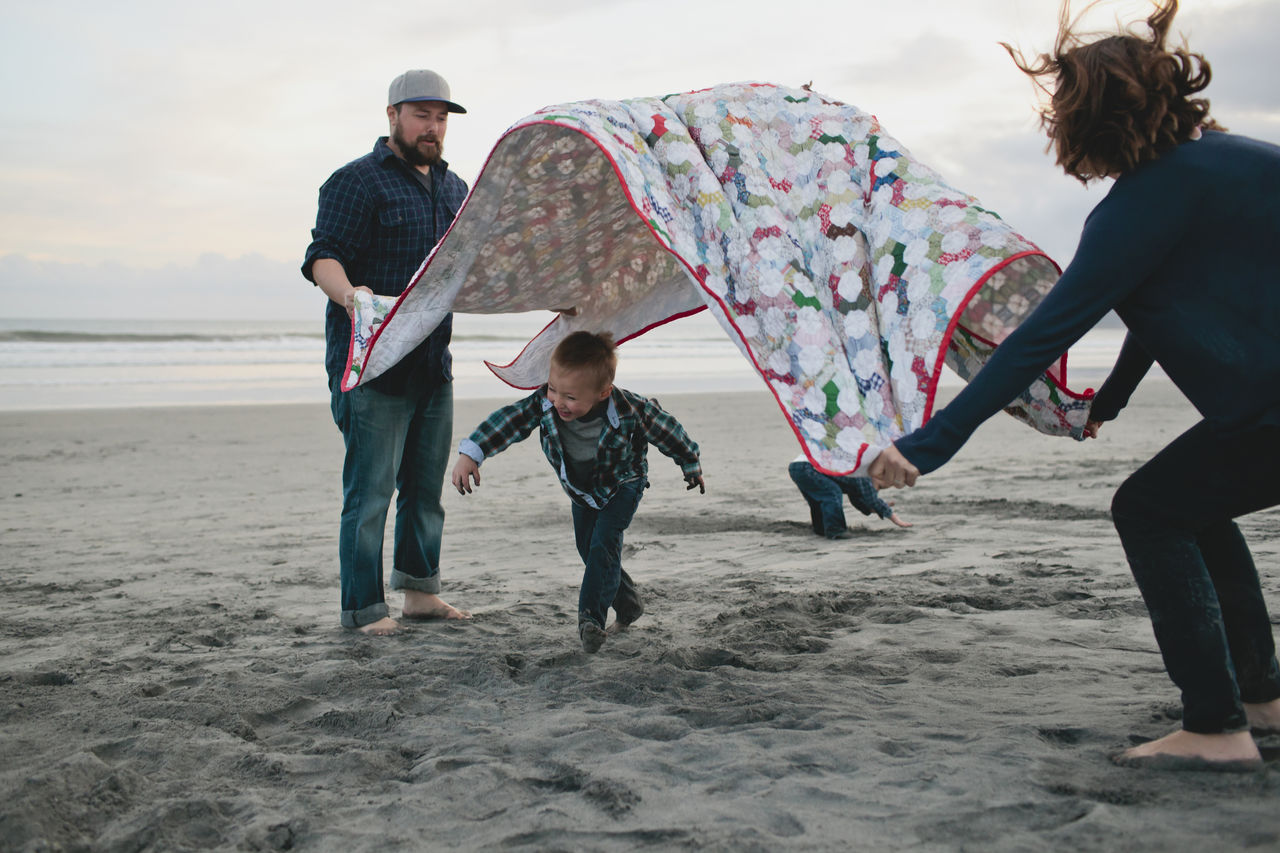 Boy running under picnic blanket held by parents at beach