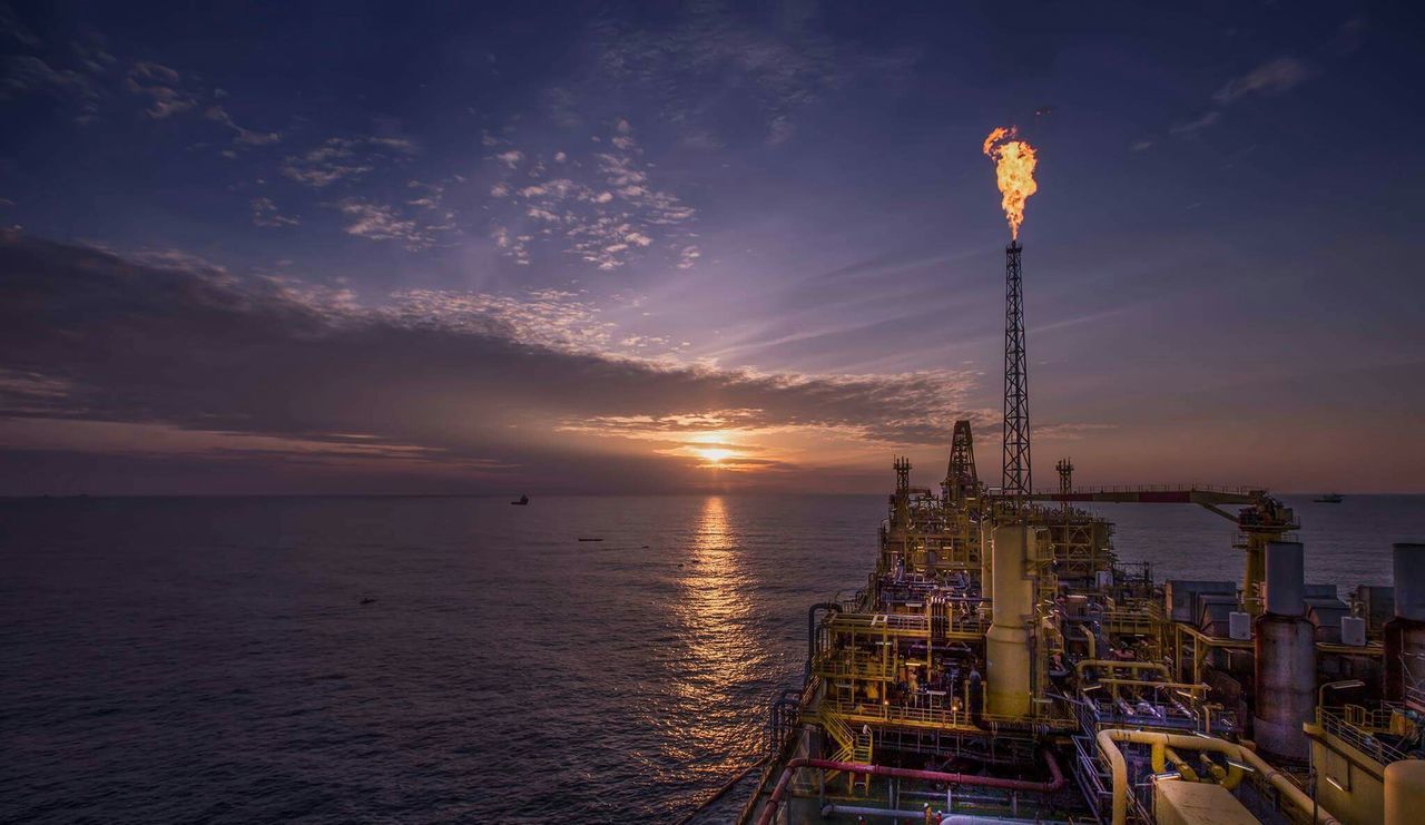 Oil rig over sea against sunset sky