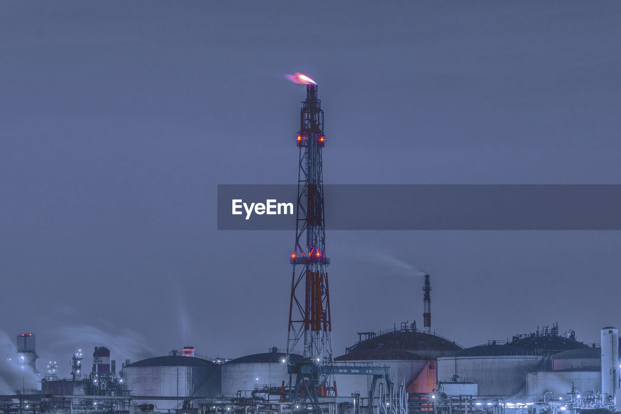 Factory in city against sky at dusk