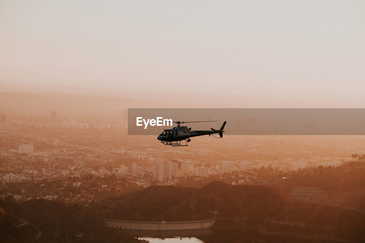 Helicopter flying over city during sunset