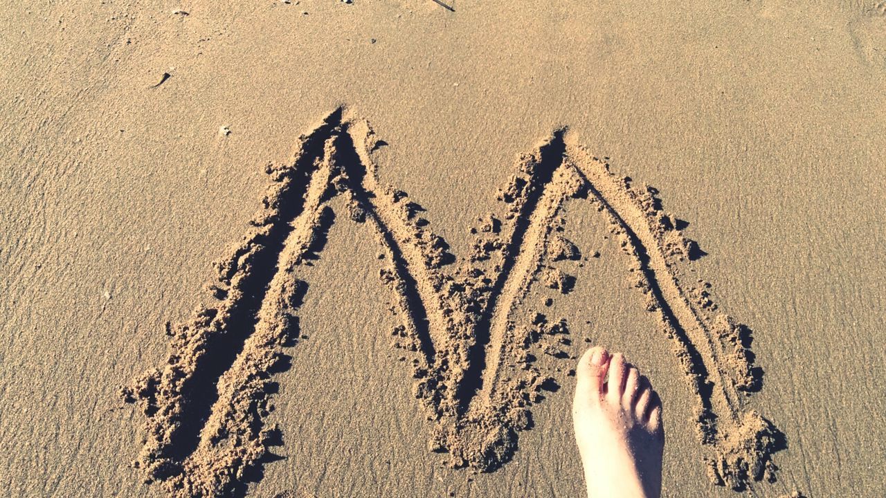 Low section of barefoot on sand by m alphabet