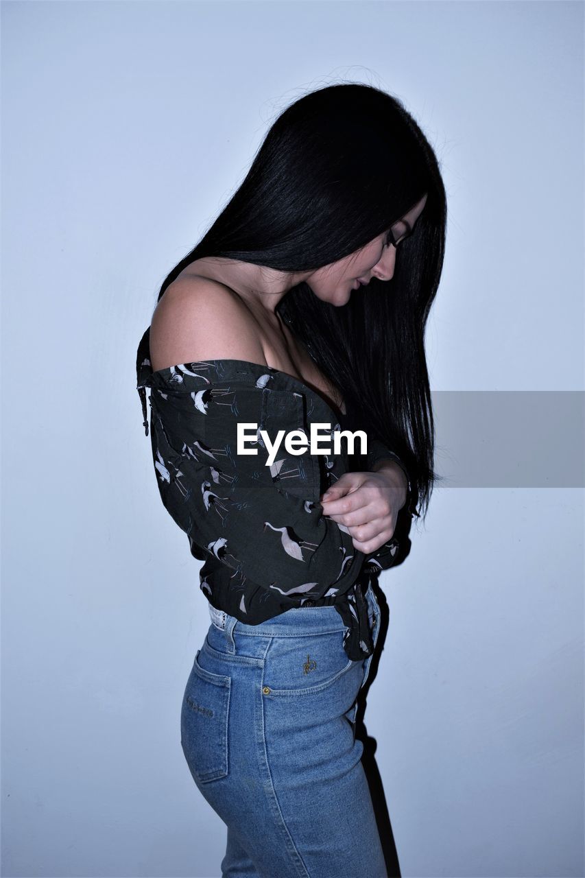 Side view of young woman standing against wall