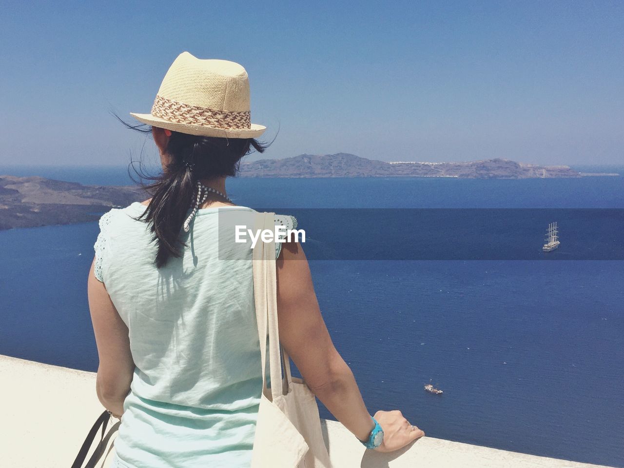 Rear view of woman standing by retaining wall against sea at santorini