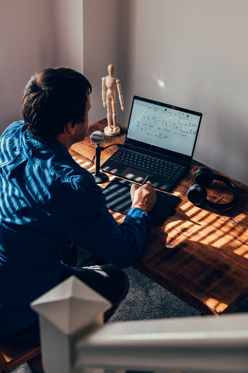 Rear view of man using laptop at table