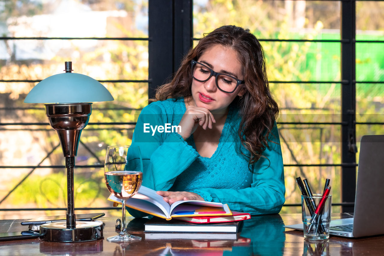 PORTRAIT OF YOUNG WOMAN SITTING ON TABLE WITH BOOK