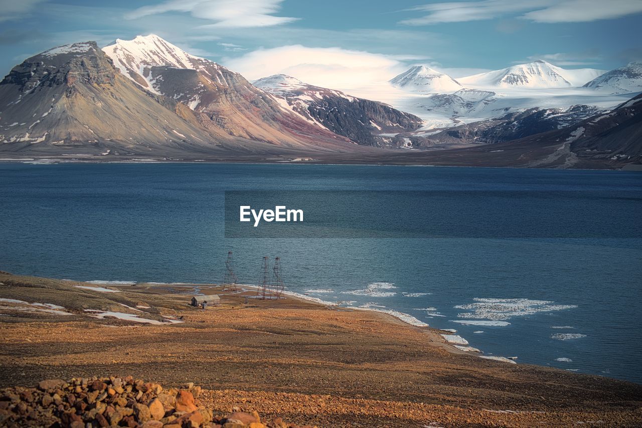 Scenic view of lake by snow covered mountains against sky
