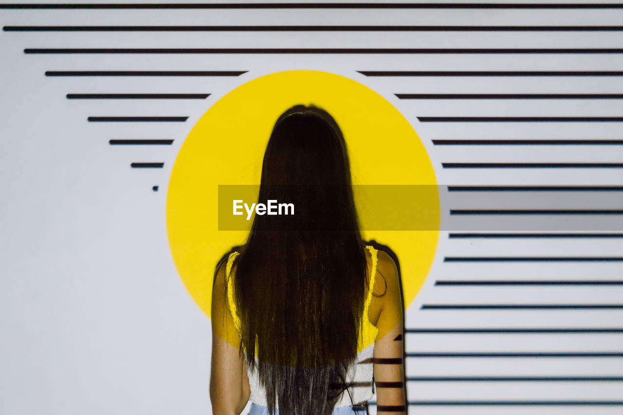 Back view of unrecognizable woman with long hair in yellow projector light with stripes