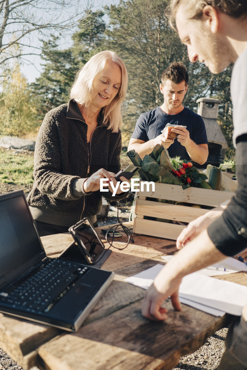 Mature woman paying male farmer through credit card at market