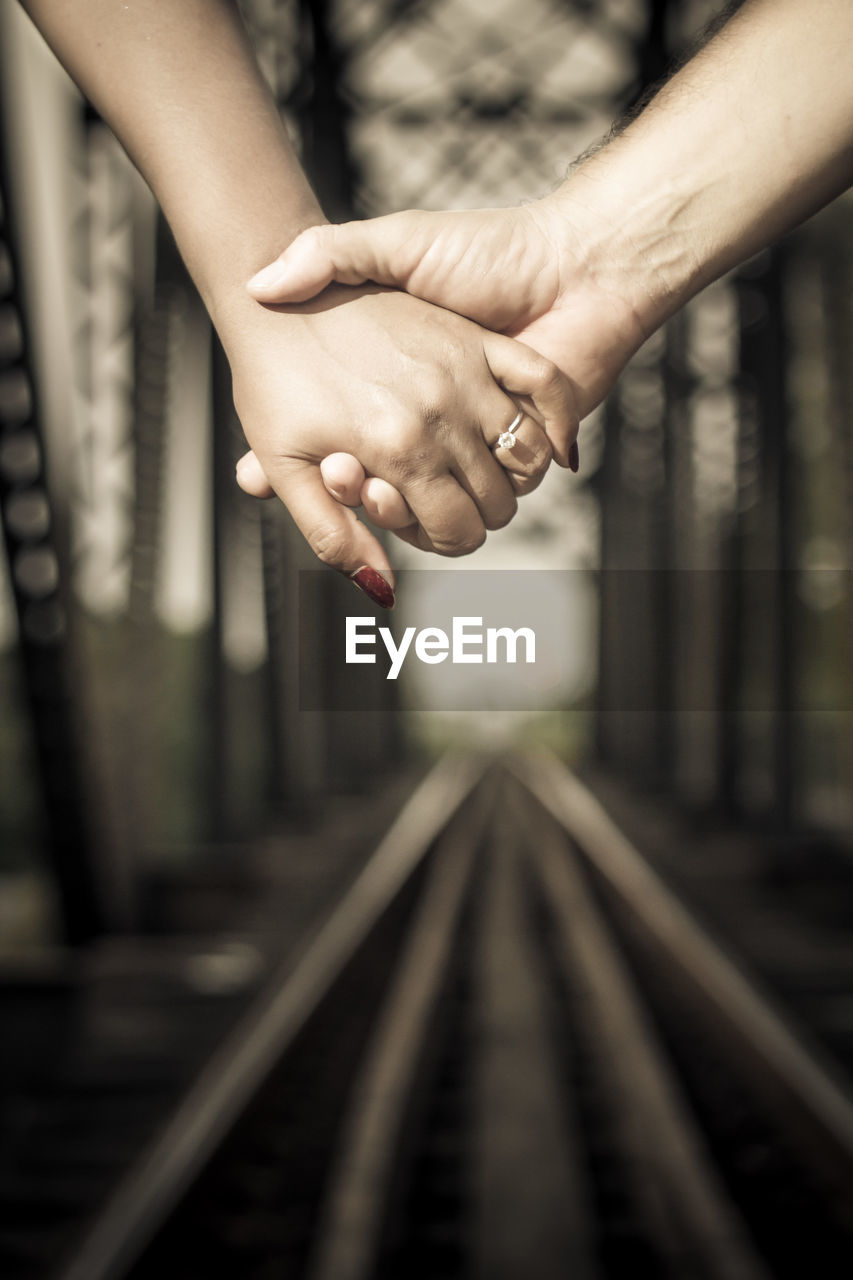 Cropped image of couple holding hands over railroad tracks