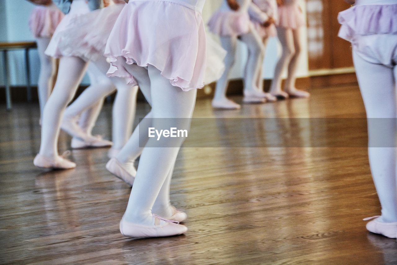 Low section of girls performing ballet on hardwood floor