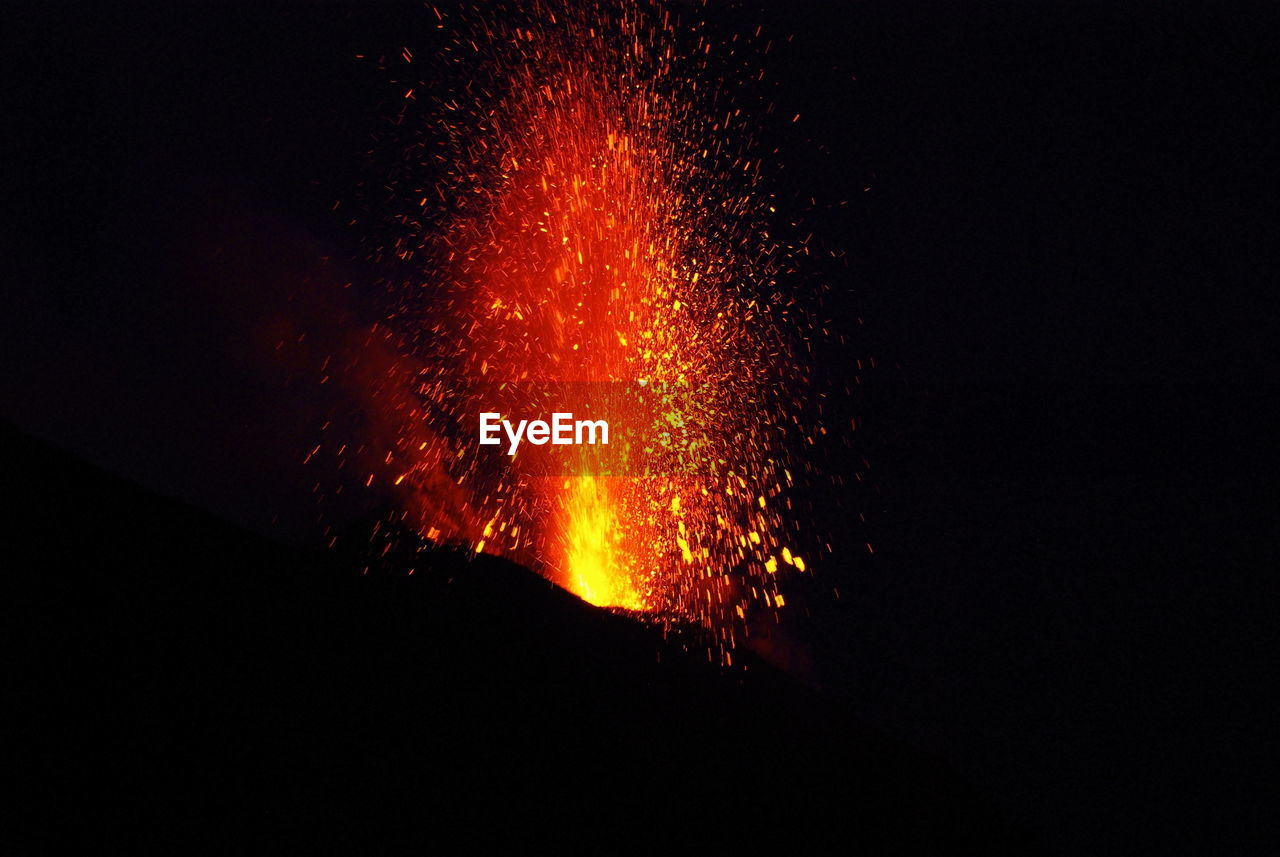 Low angle view of lava erupting at silhouette mountain