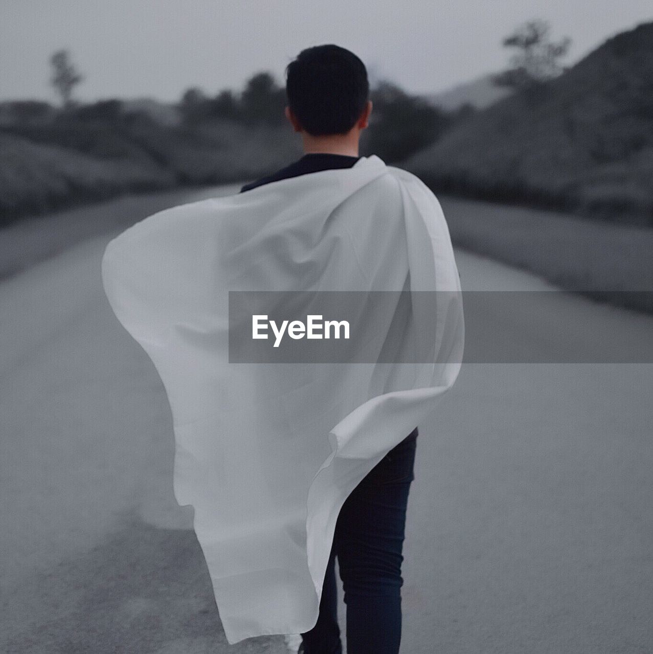 Rear view of man with white sheet walking on road