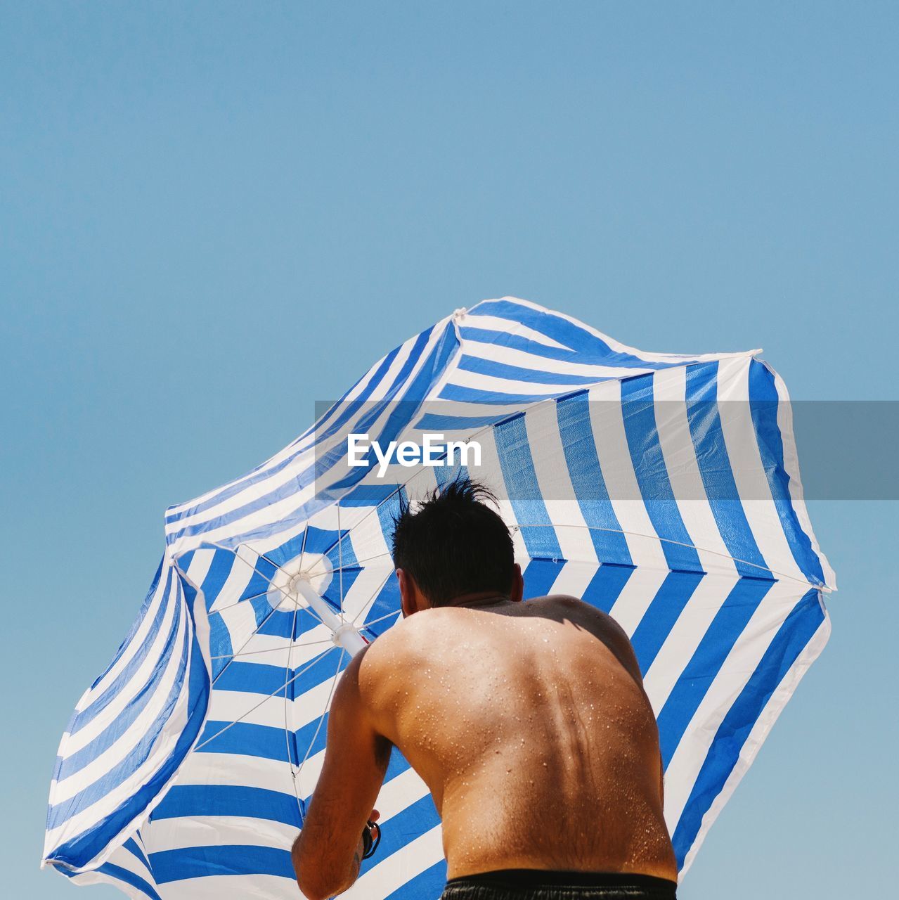 Low angle view of person holding beach umbrella against clear blue sky