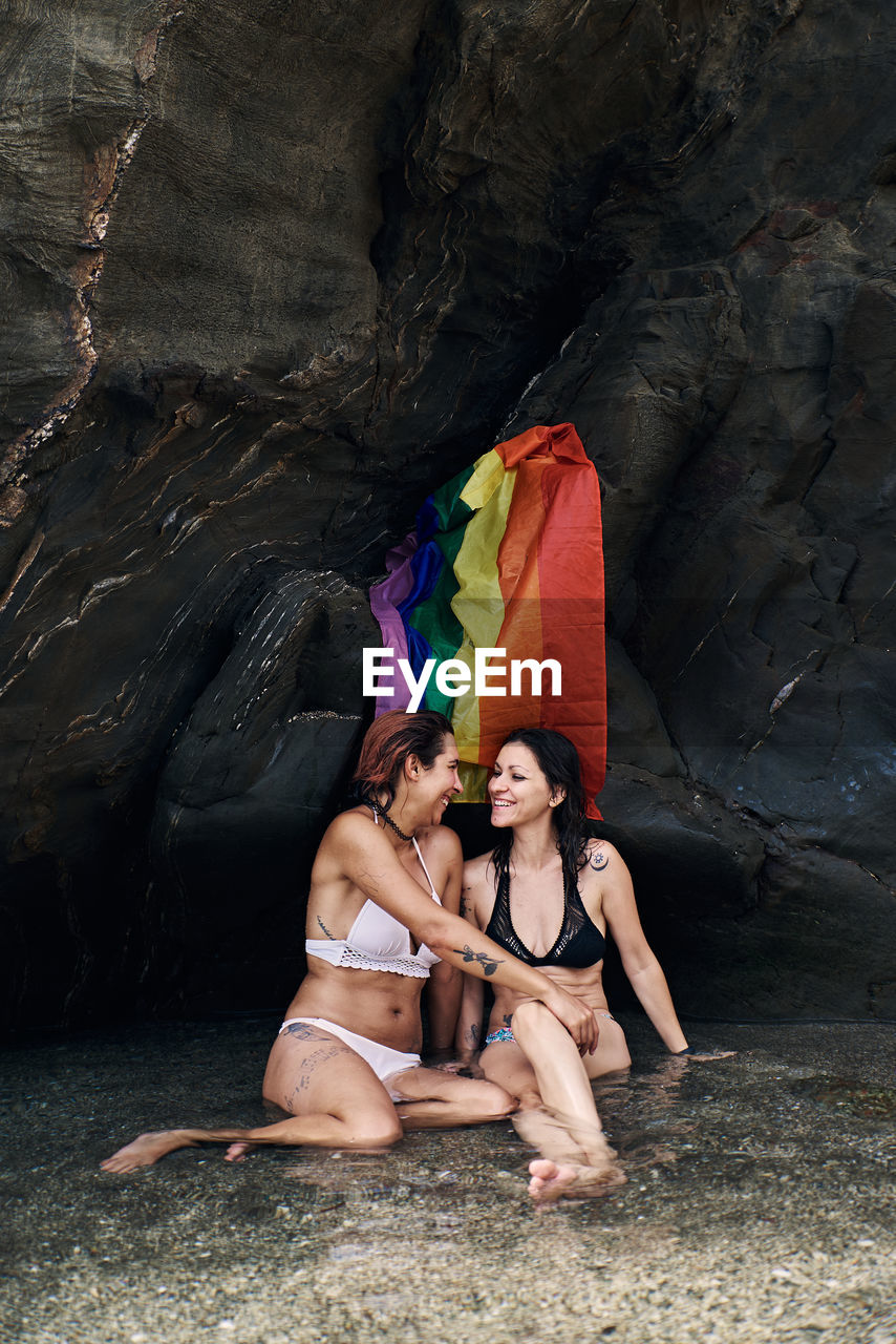 Two girls in bikinis on the seashore with the gay flag. holiday and gay concept
