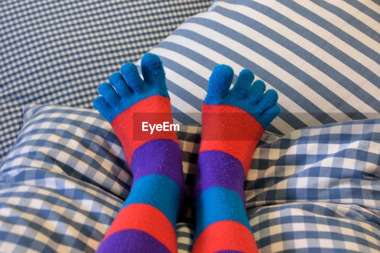 Low section of person wearing colorful socks on bed