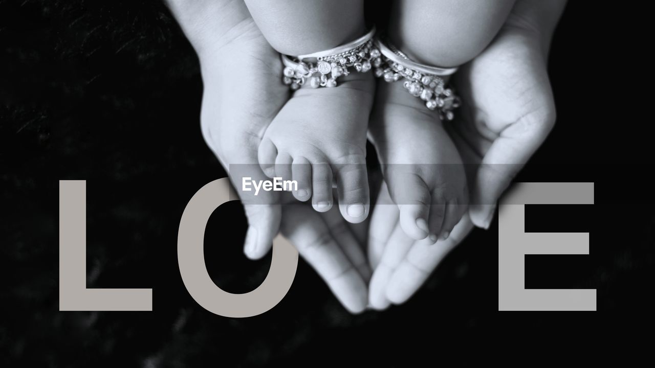 Cropped hands holding feet of baby against love text on black background