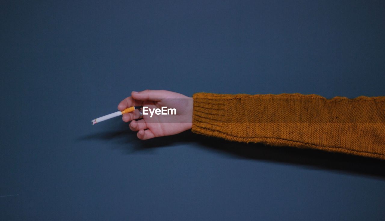 Close-up of hand holding cigarette over gray background