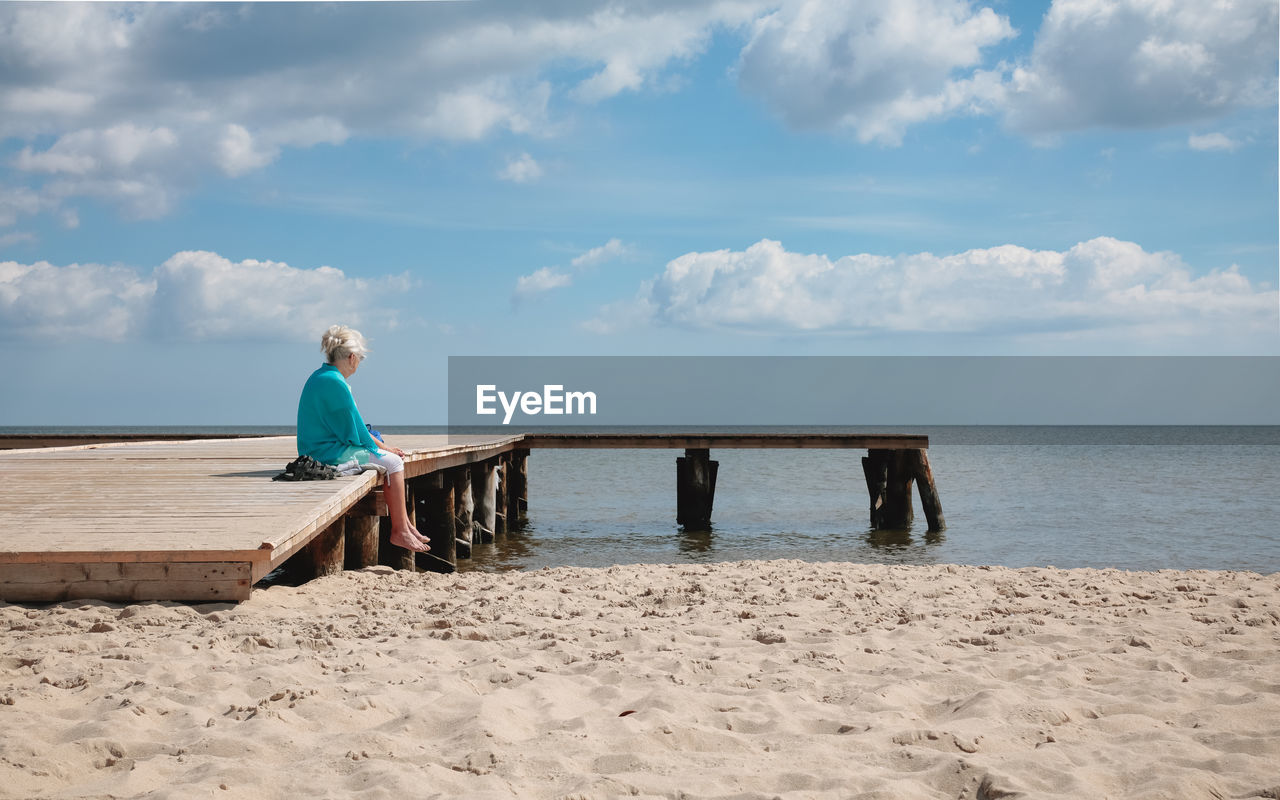 Old woman at the beach, sitting at the dock looking at the horizon.