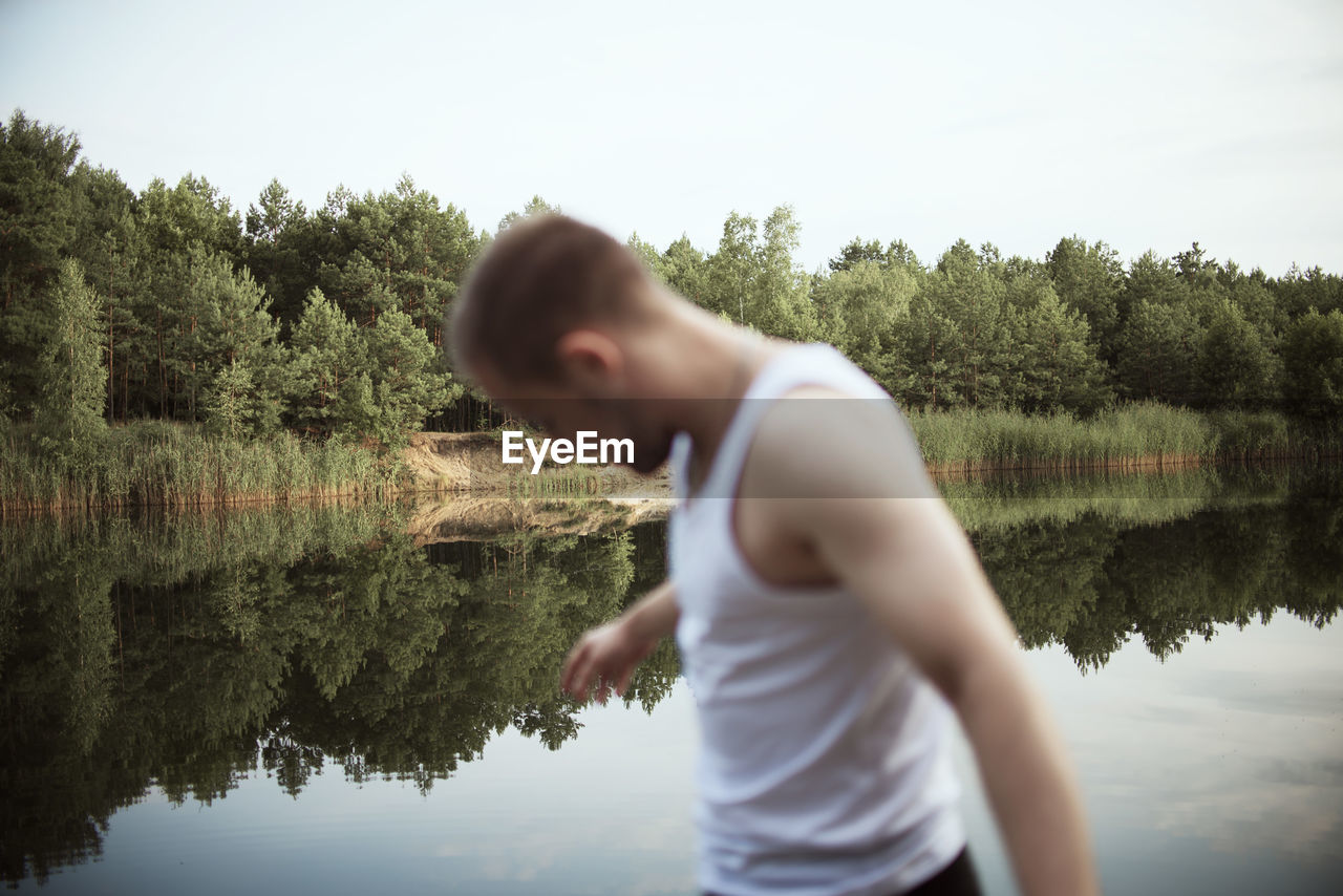 Side view of man standing by lake against sky