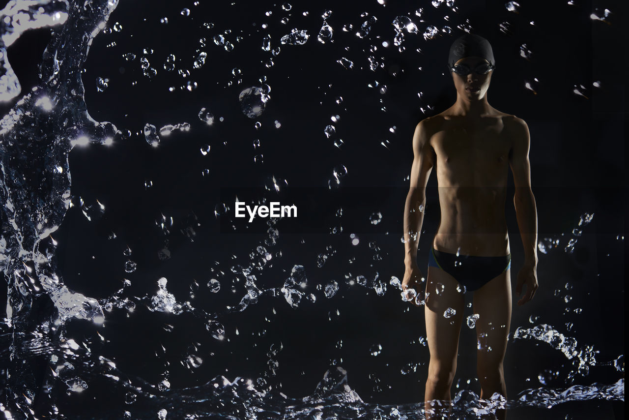 Water splashing against shirtless swimmer against black background