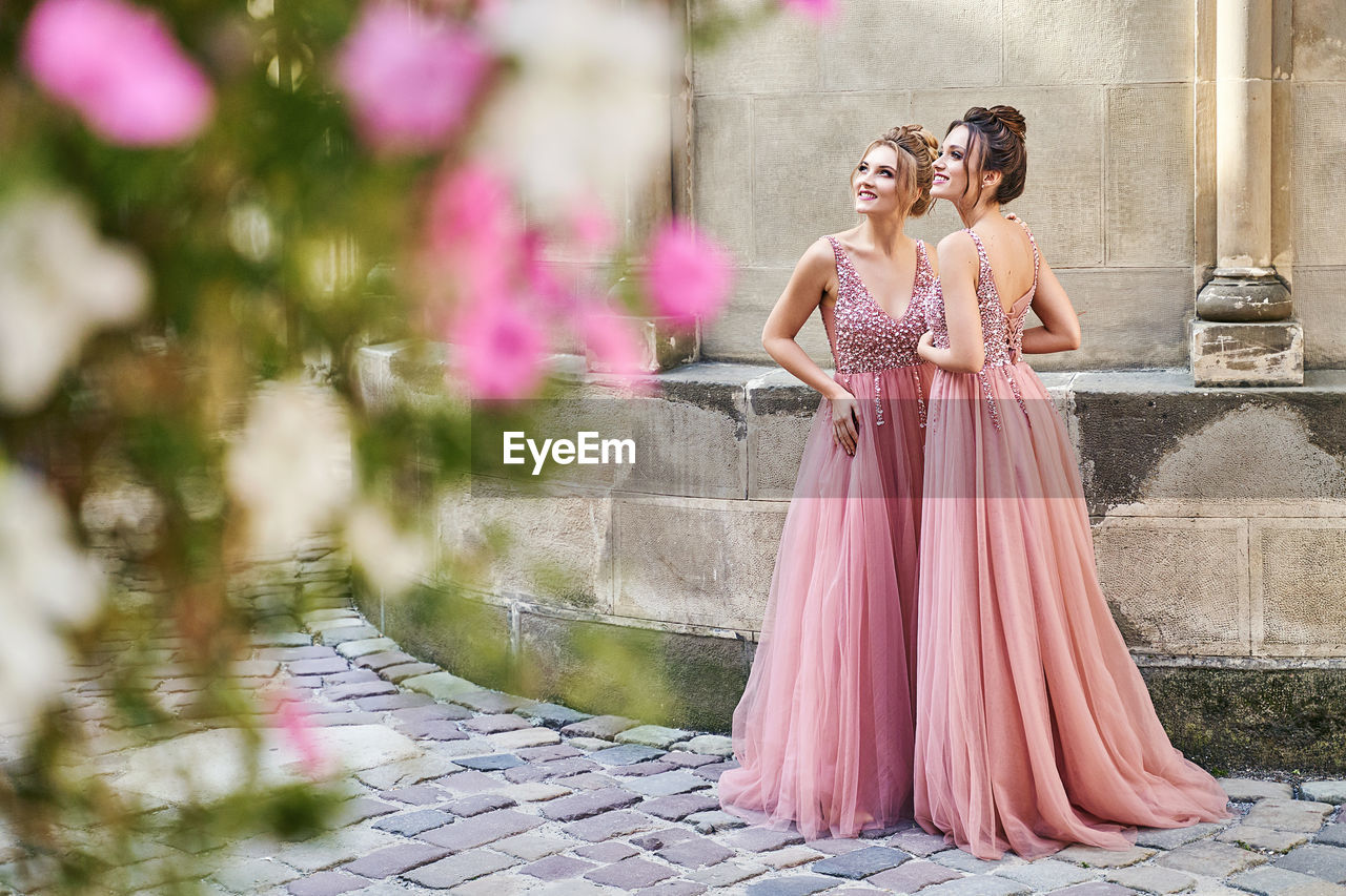 Beautiful bridesmaids in elegant pink floor-length dress holding flowers bouquets. 