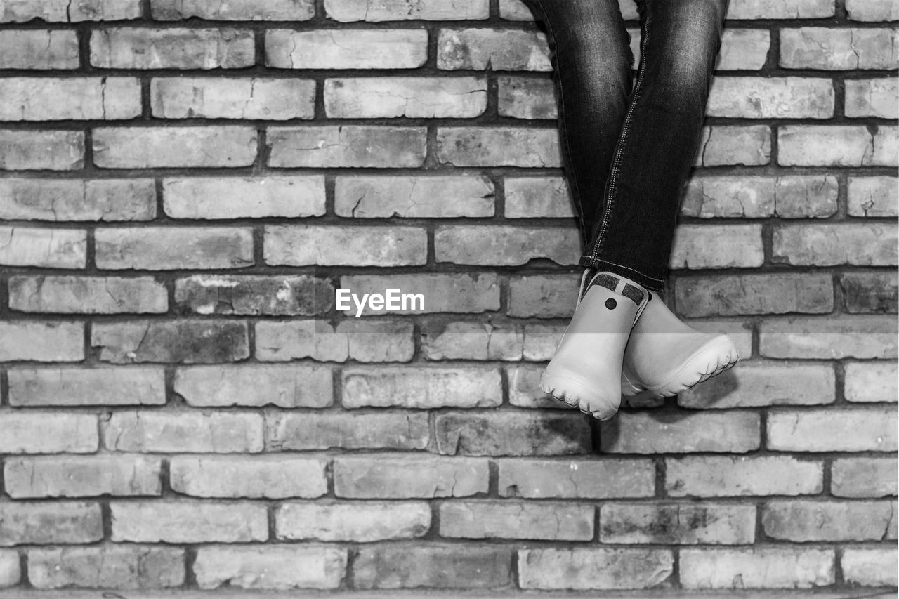 Crossed legs of a young girl in jeans and galoshes sitting on a brick wall