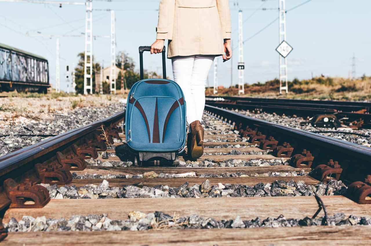 Woman's legs walking with her suitcase along a railway track.
