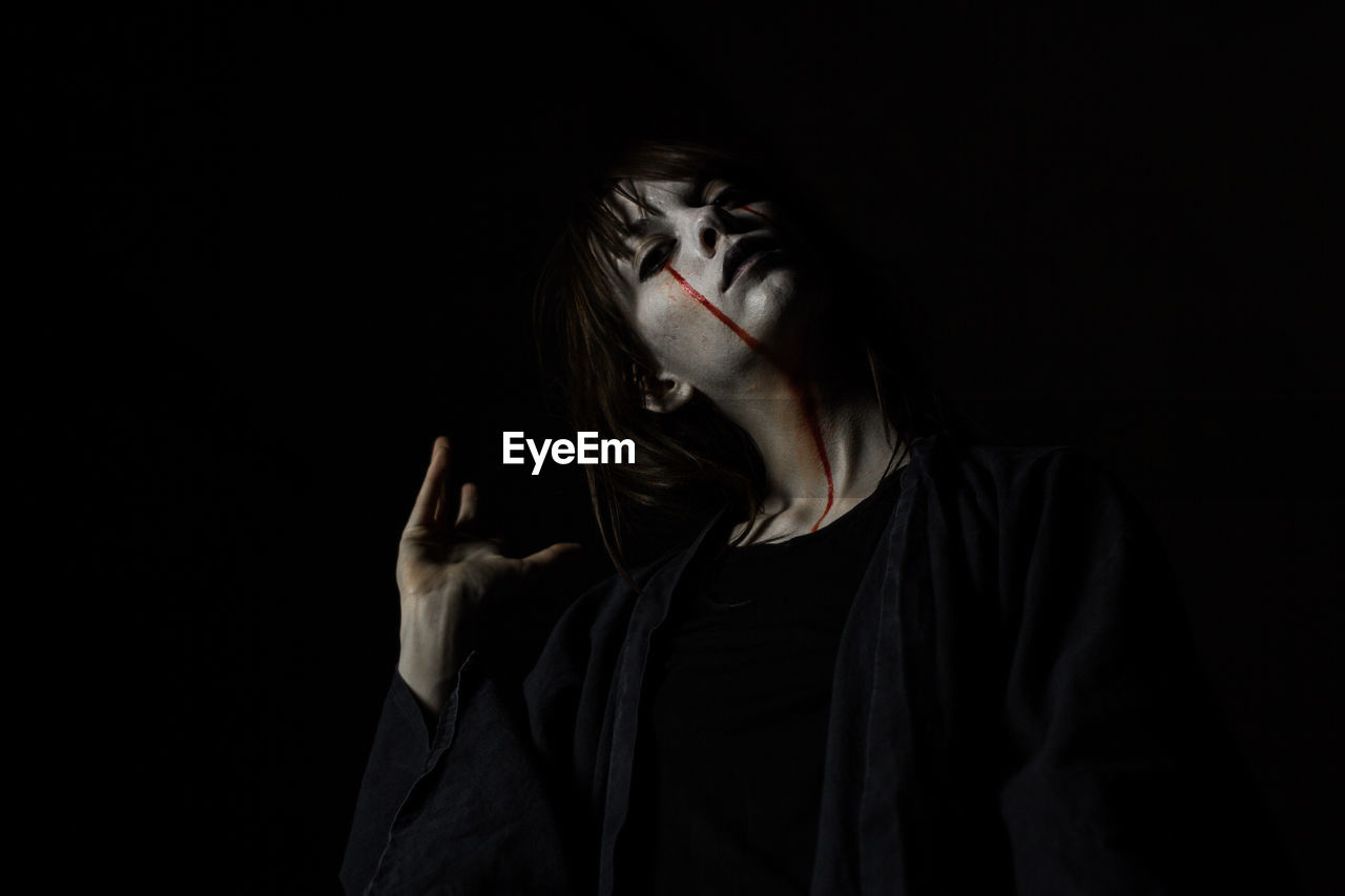 Portrait of young woman with halloween make-up against black background