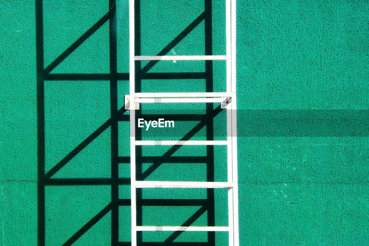 Close-up of metal ladder against green stucco wall