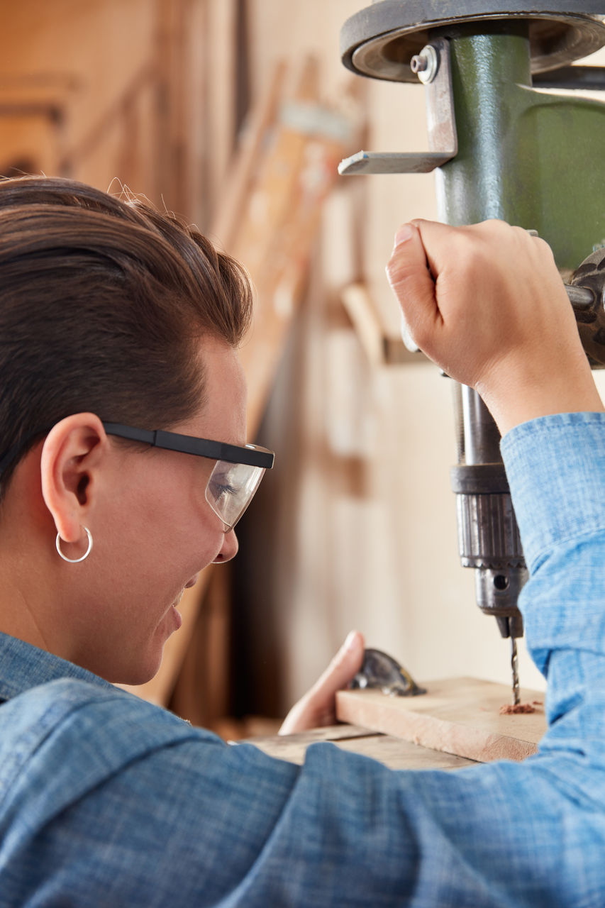 Close-up of smiling carpenter using drill at workshop