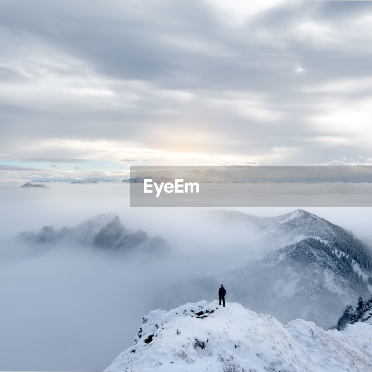 Person standing on snowcapped mountain against cloudy sky
