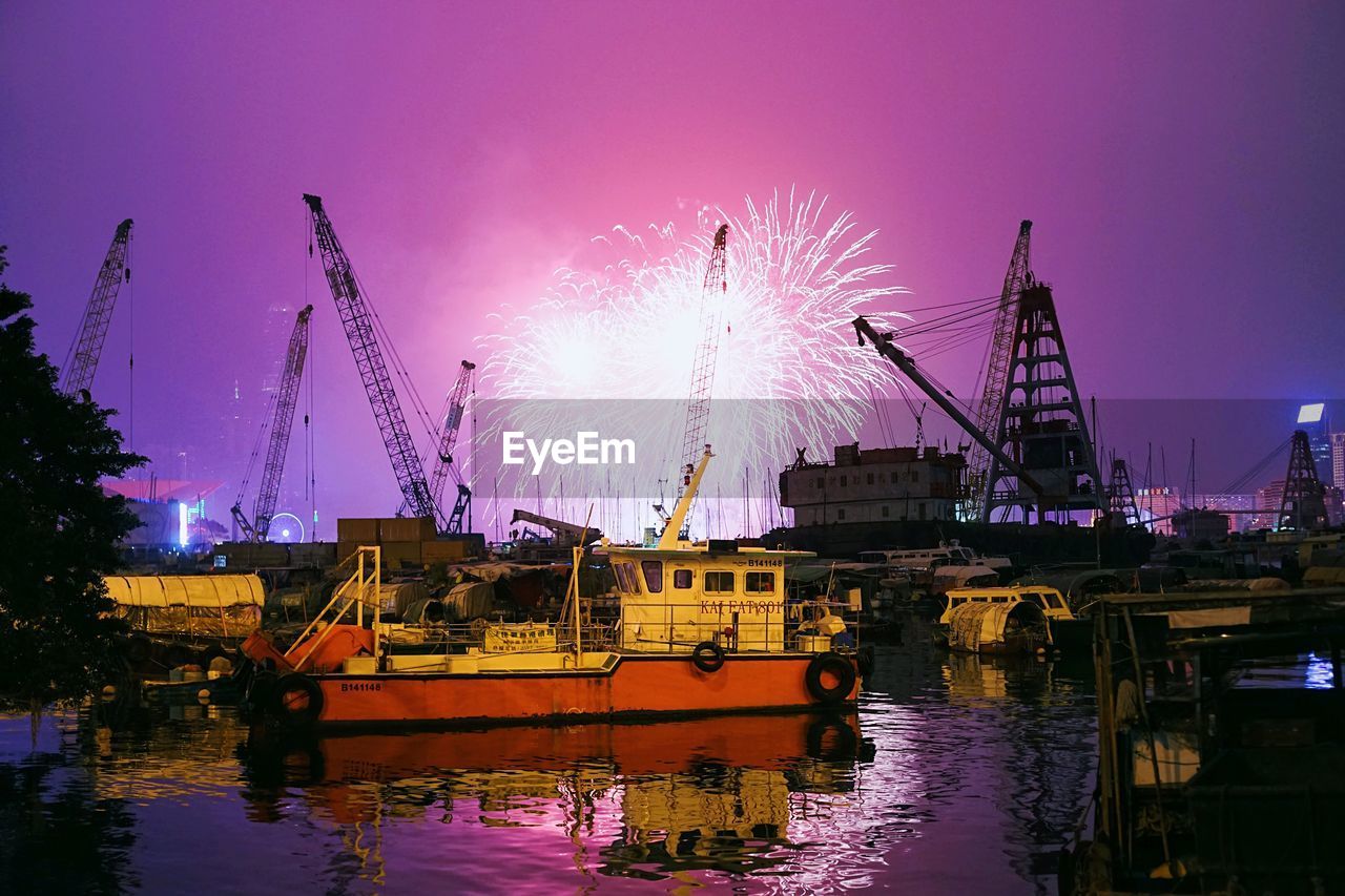 Firework display over cranes and boats by river