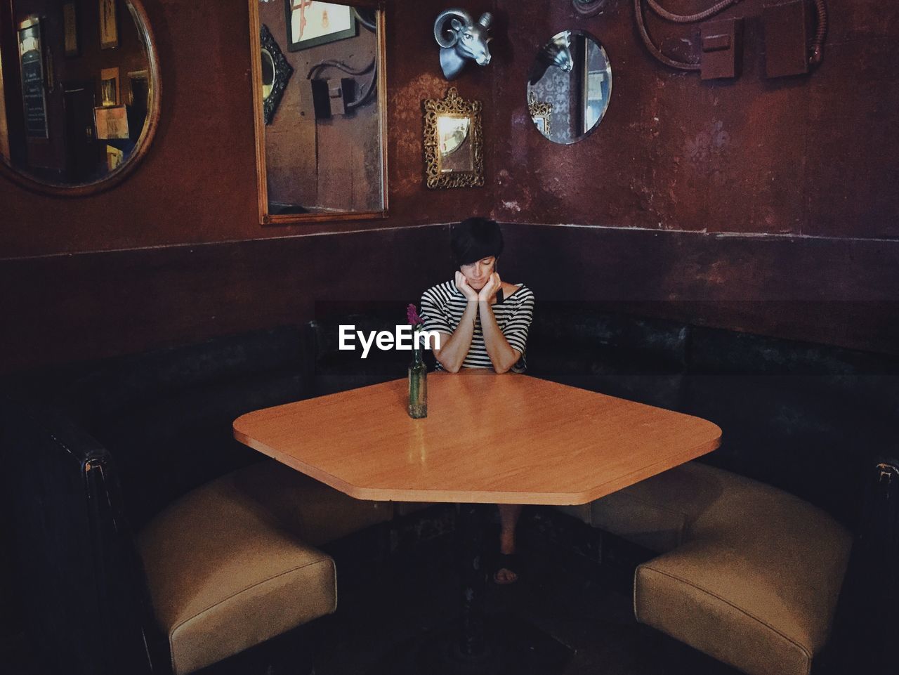 Depressed young woman with hands on chin sitting in restaurant