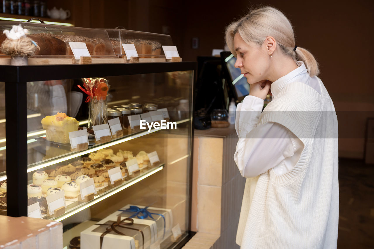 A cute girl stands at the window in a pastry shop and chooses a dessert