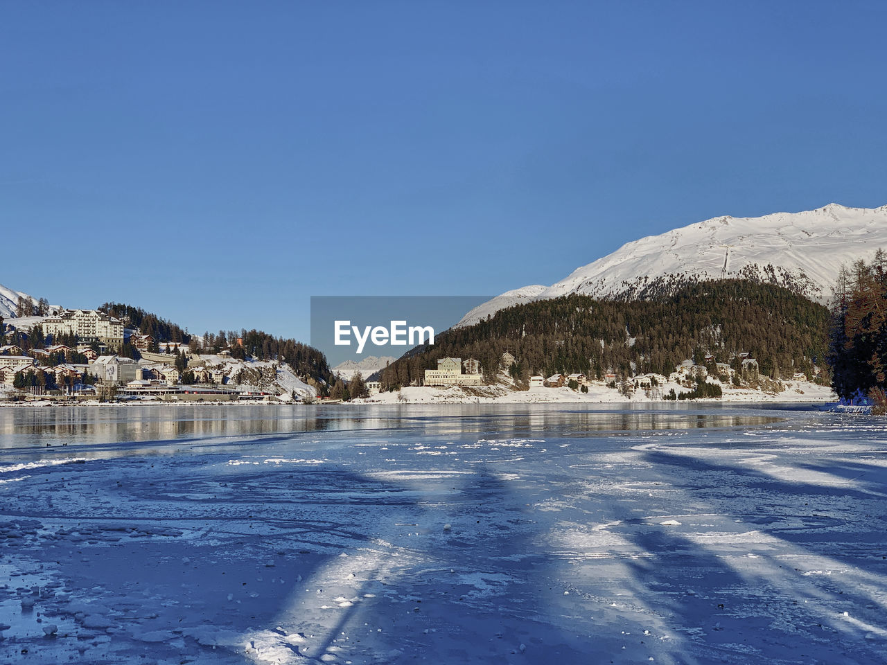 Scenic view of frozen lake by snowcapped mountains against clear blue sky