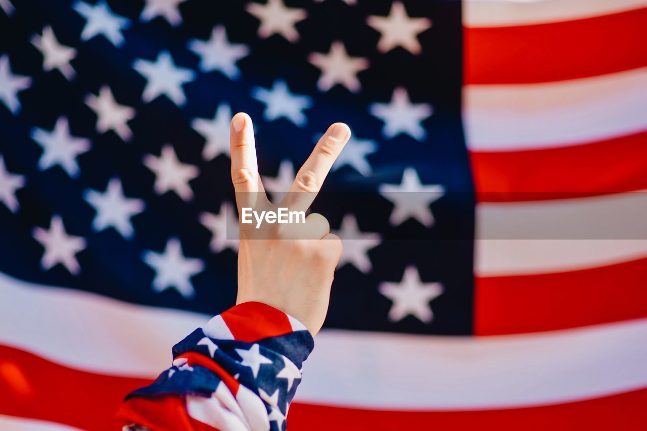 Cropped image of hand showing peace sign against american flag