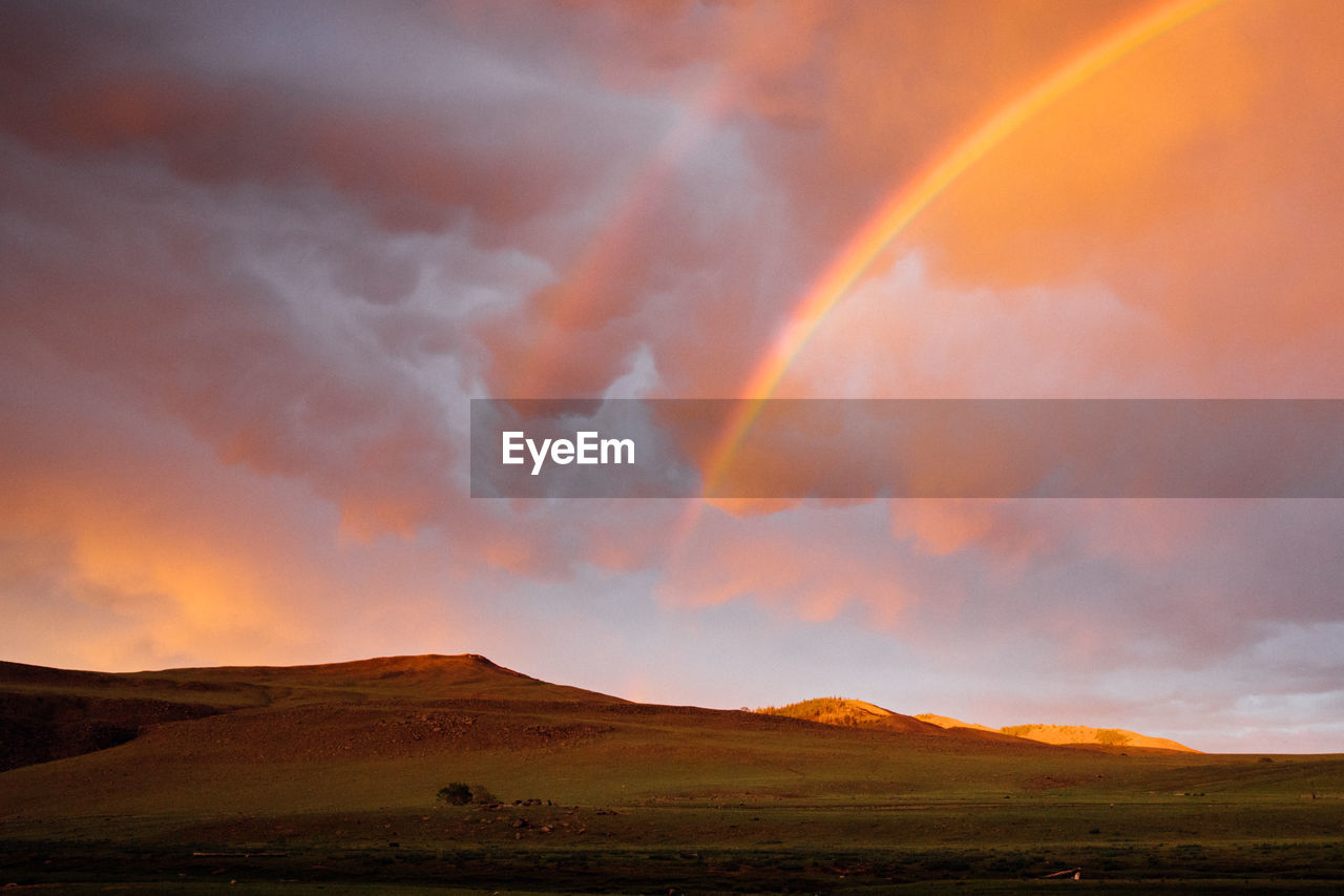 SCENIC VIEW OF RAINBOW OVER LAND AGAINST SKY DURING SUNSET