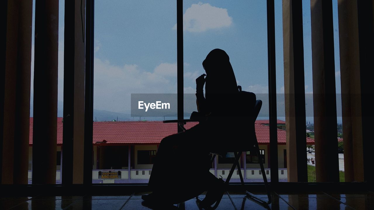 SIDE VIEW OF SILHOUETTE WOMAN STANDING BY WINDOW