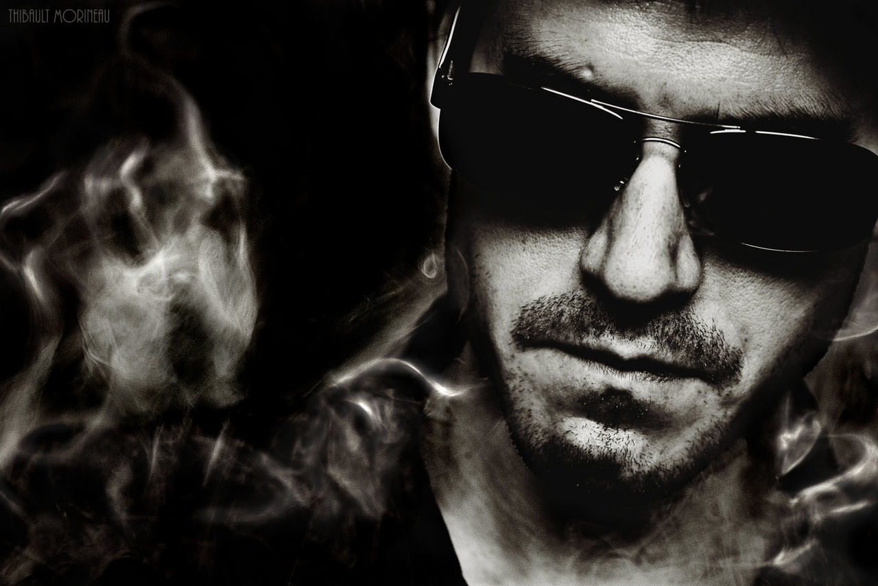 Close-up of young man wearing sunglasses surrounded by smoke against black background