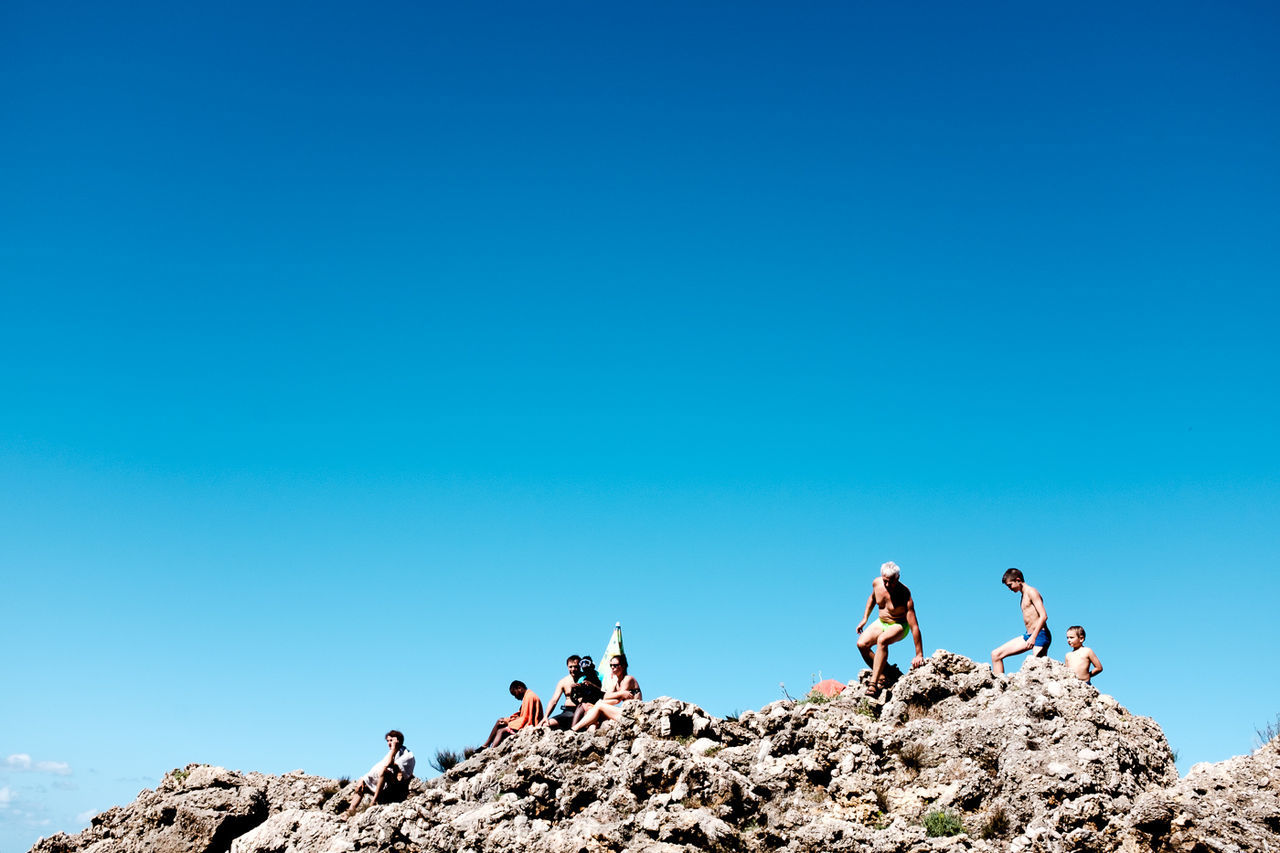 People on rocks against clear blue sky