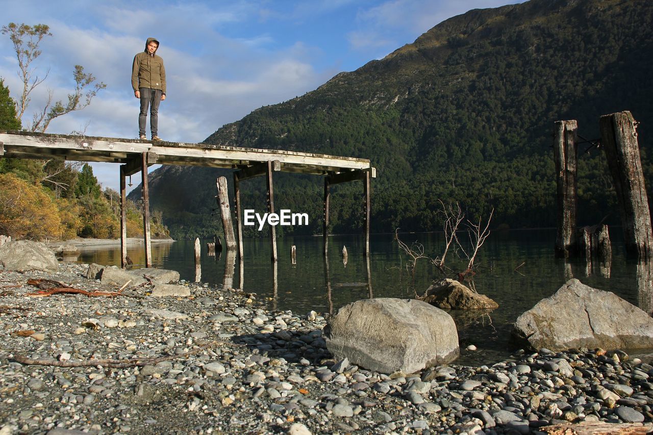 Man standing on pier over lake against mountain