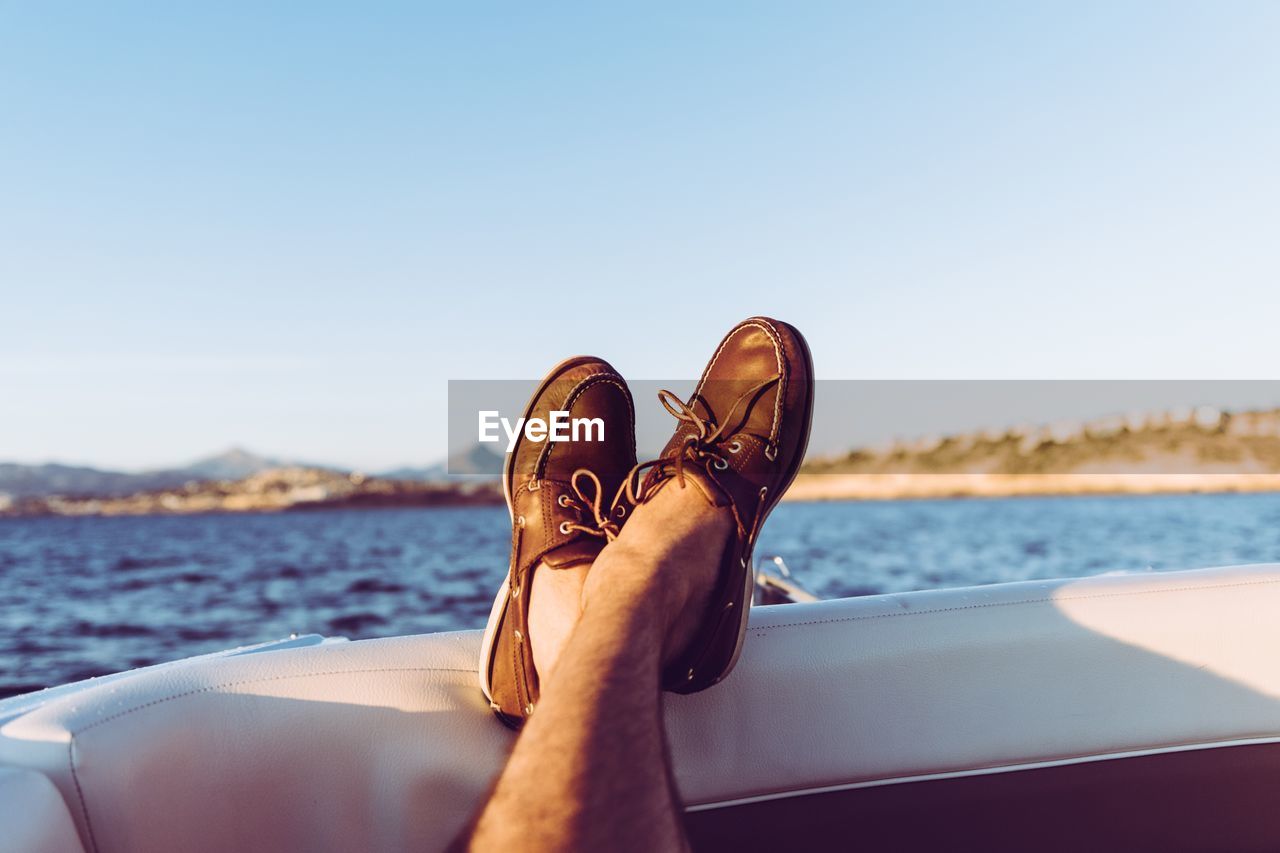 Low section of man wearing shoes resting on boat in sea