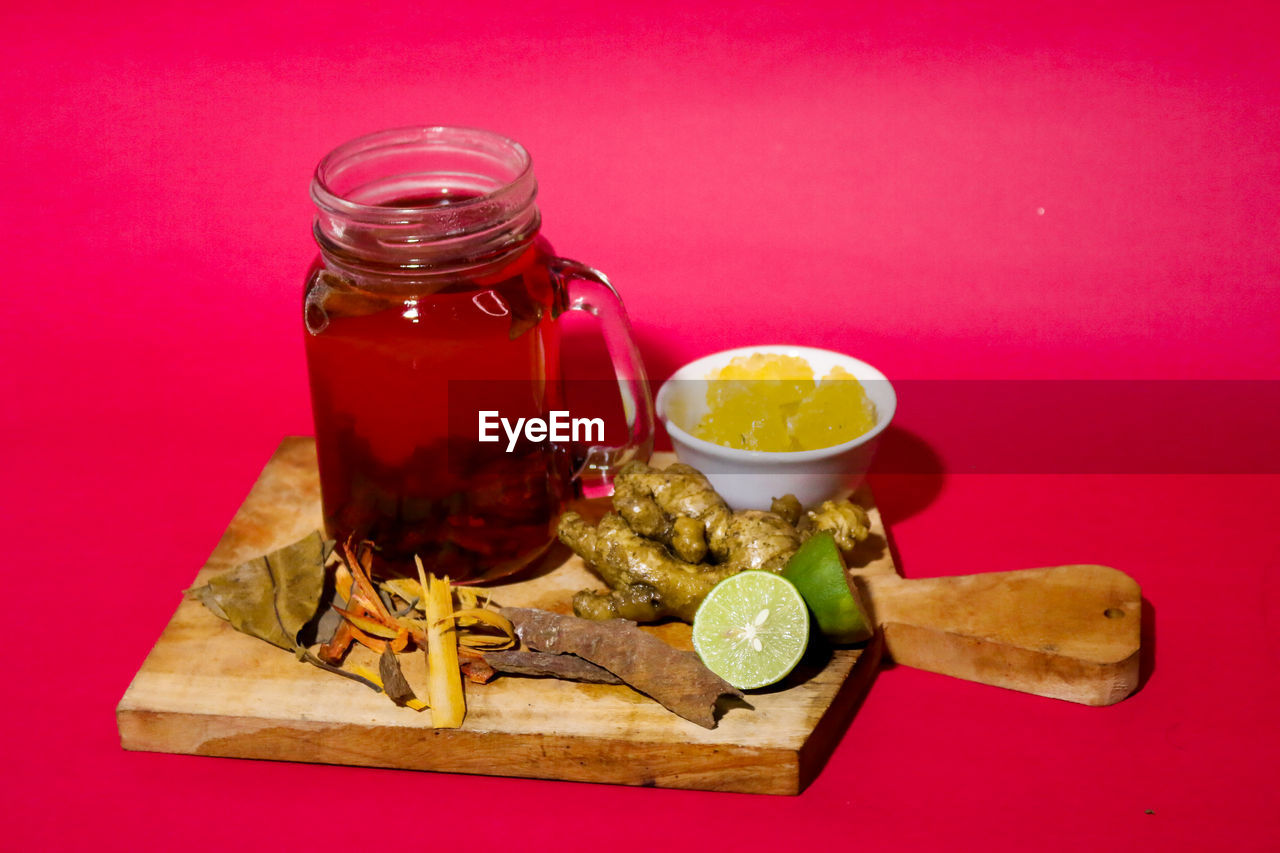 CLOSE-UP OF DRINK IN JAR ON TABLE AGAINST RED BACKGROUND