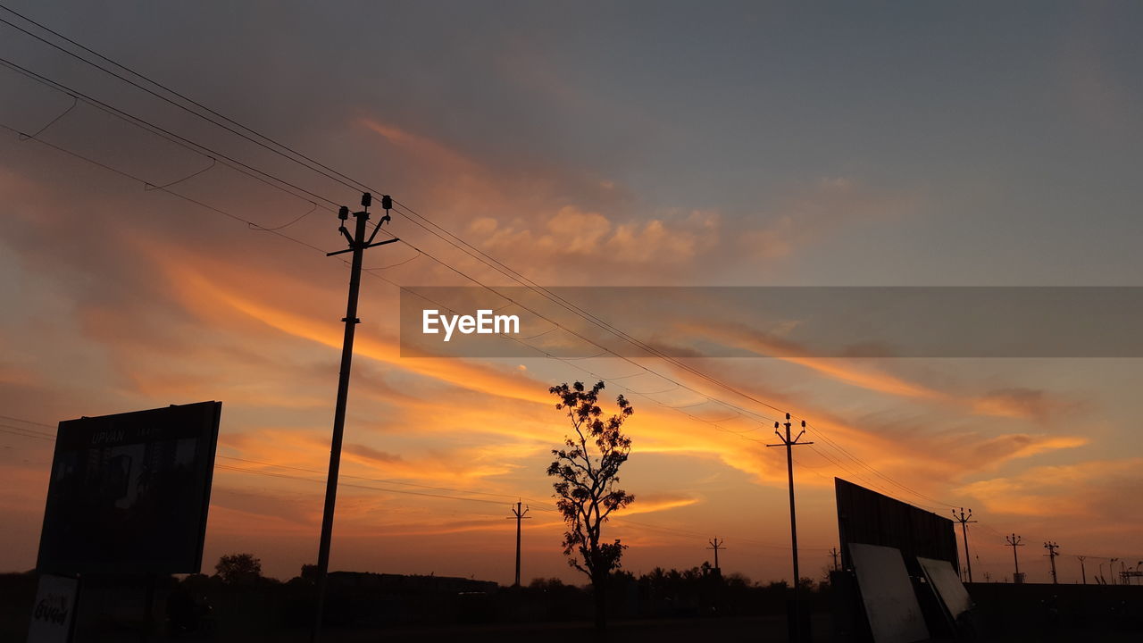 LOW ANGLE VIEW OF SILHOUETTE ELECTRICITY PYLONS AGAINST ORANGE SKY