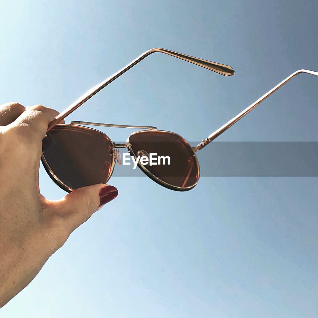 Cropped woman hand holding sunglasses against clear sky