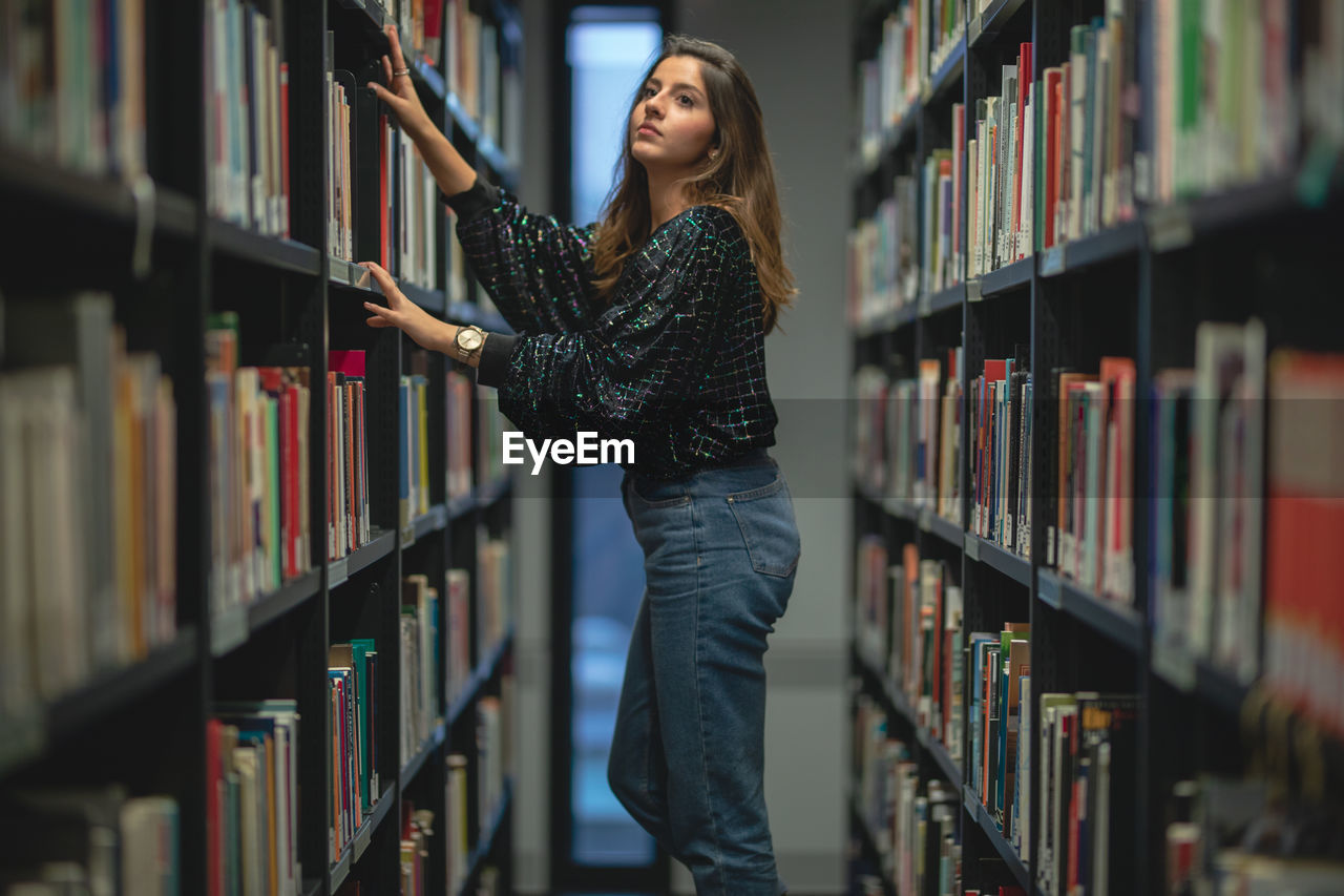 Side view of young woman looking at books in library