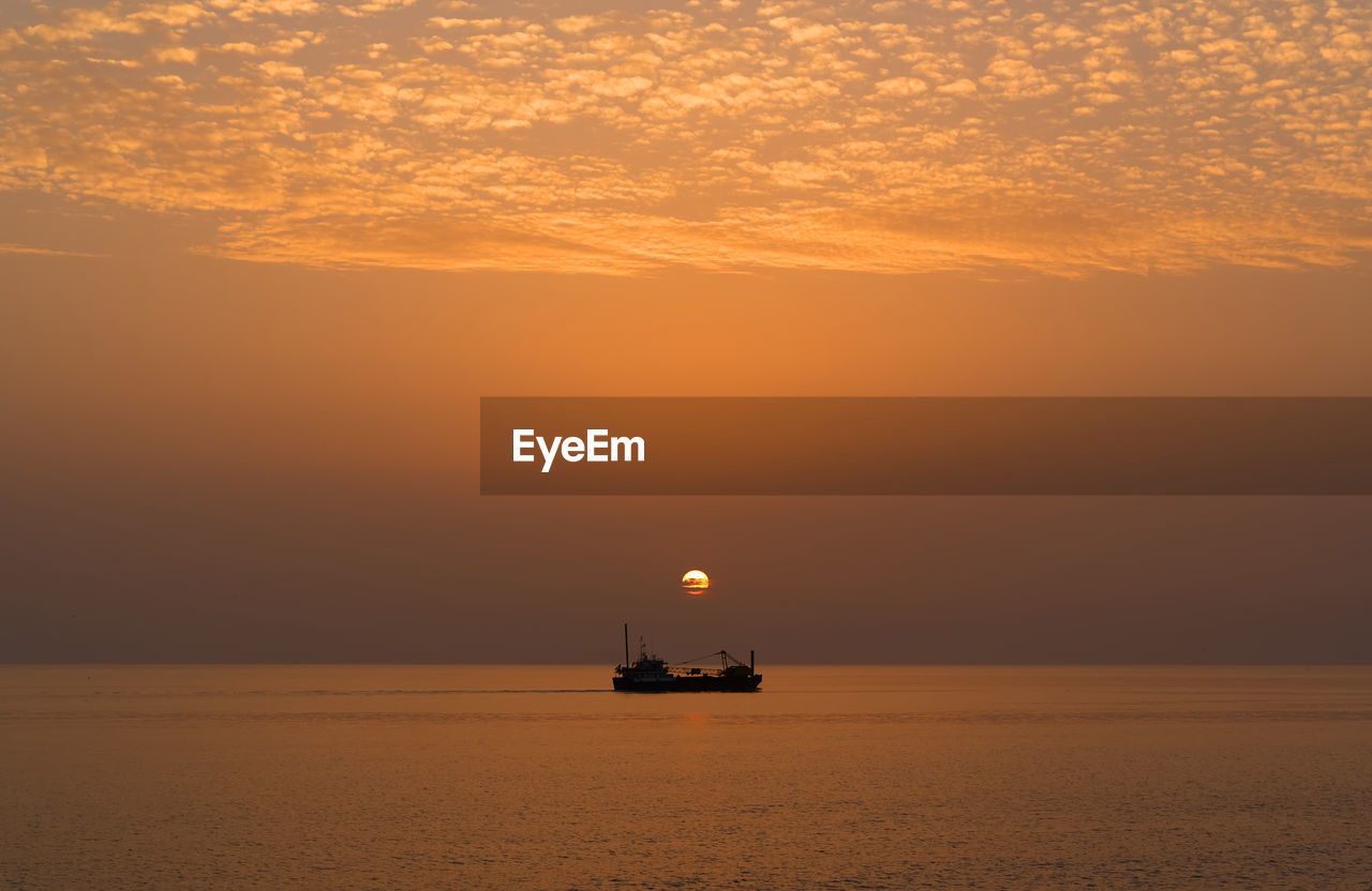 Scenic view of sea against orange sky with a boat
